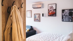 Habitació amb una estant de fusta on hi ha una tovallola beix, un llit amb roba de llit blanca i diverses fotos amb marc a la paret.