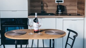 Una cuina moderna amb taulell de fusta, fornell i cafetera. Hi ha una taula rodona amb dues cadires i una ampolla de vi a sobre.
