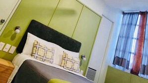 A bed with a black headboard, white and patterned pillows, and a green bedspread. - Lu De Anda (San Luis Potosi)