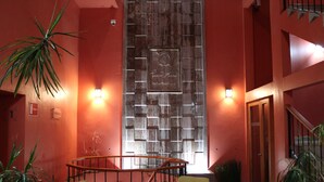A lobby with a wooden wall, green chairs, a wooden table, and potted plants. - Lu De Anda (San Luis Potosi)