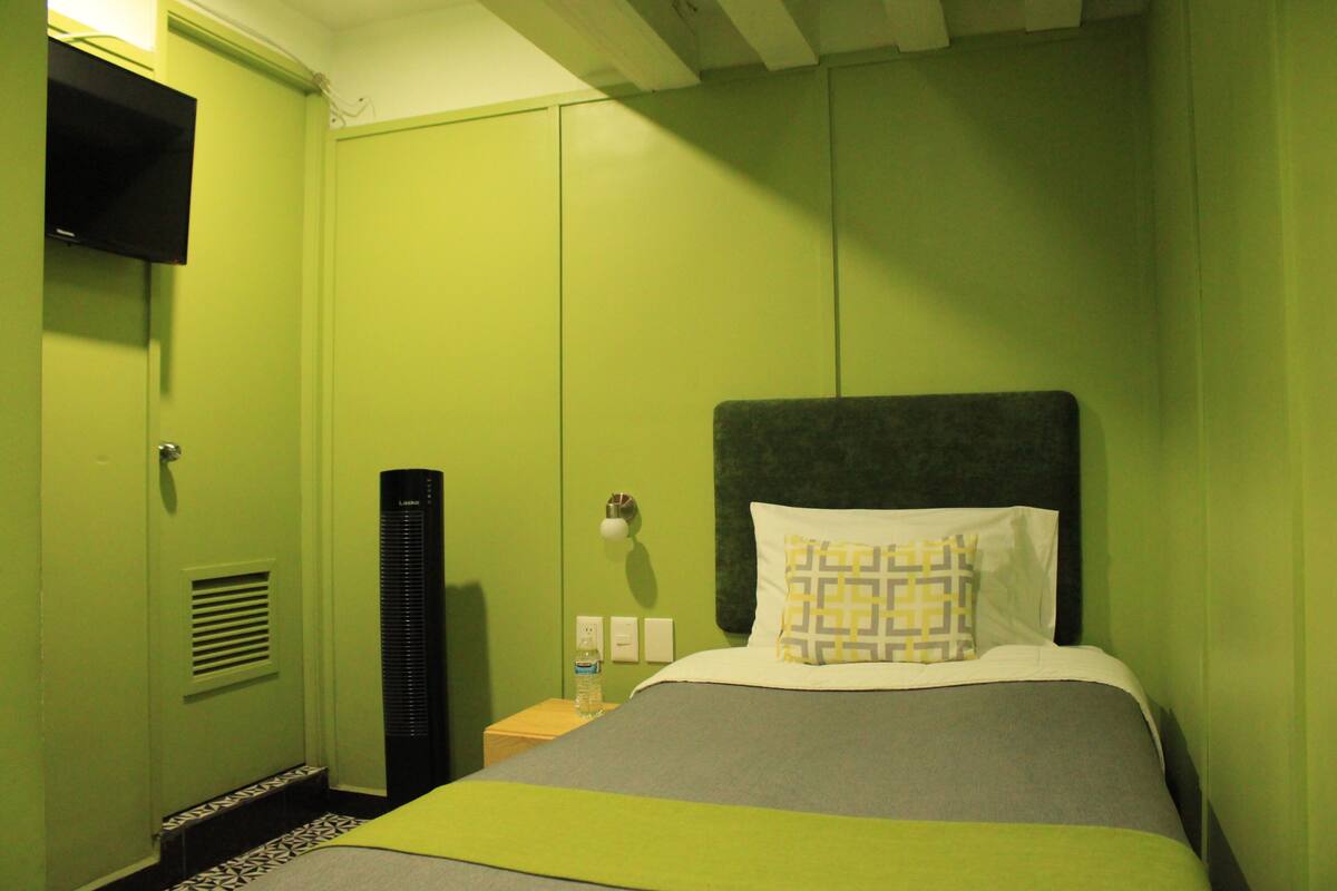 Een hotelkamer met een bed, nachtkastje, verwarming en een aan de muur bevestigde televisie.