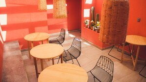 A room with round wooden tables and black wireframe chairs, a wicker hanging chair, and a cactus plant on the wall. - Lu De Anda (San Luis Potosi)