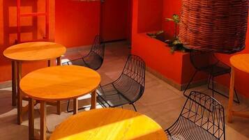 A modern interior with wooden beams, red walls, and wicker hanging lamps. There are round tables and metal chairs.