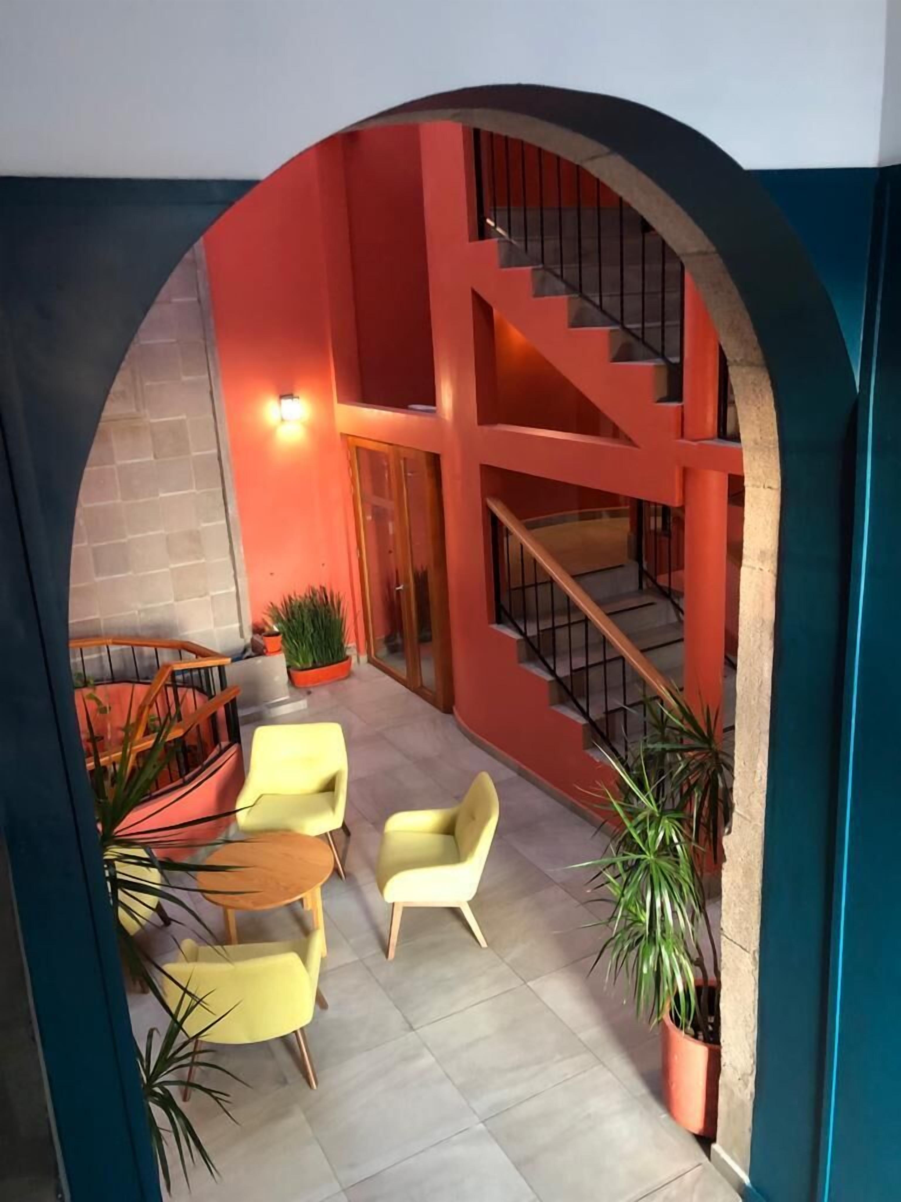 Un interior moderno con una paleta de colores rojo y azul, que incluye una escalera, zona de estar con sillas y plantas en macetas.