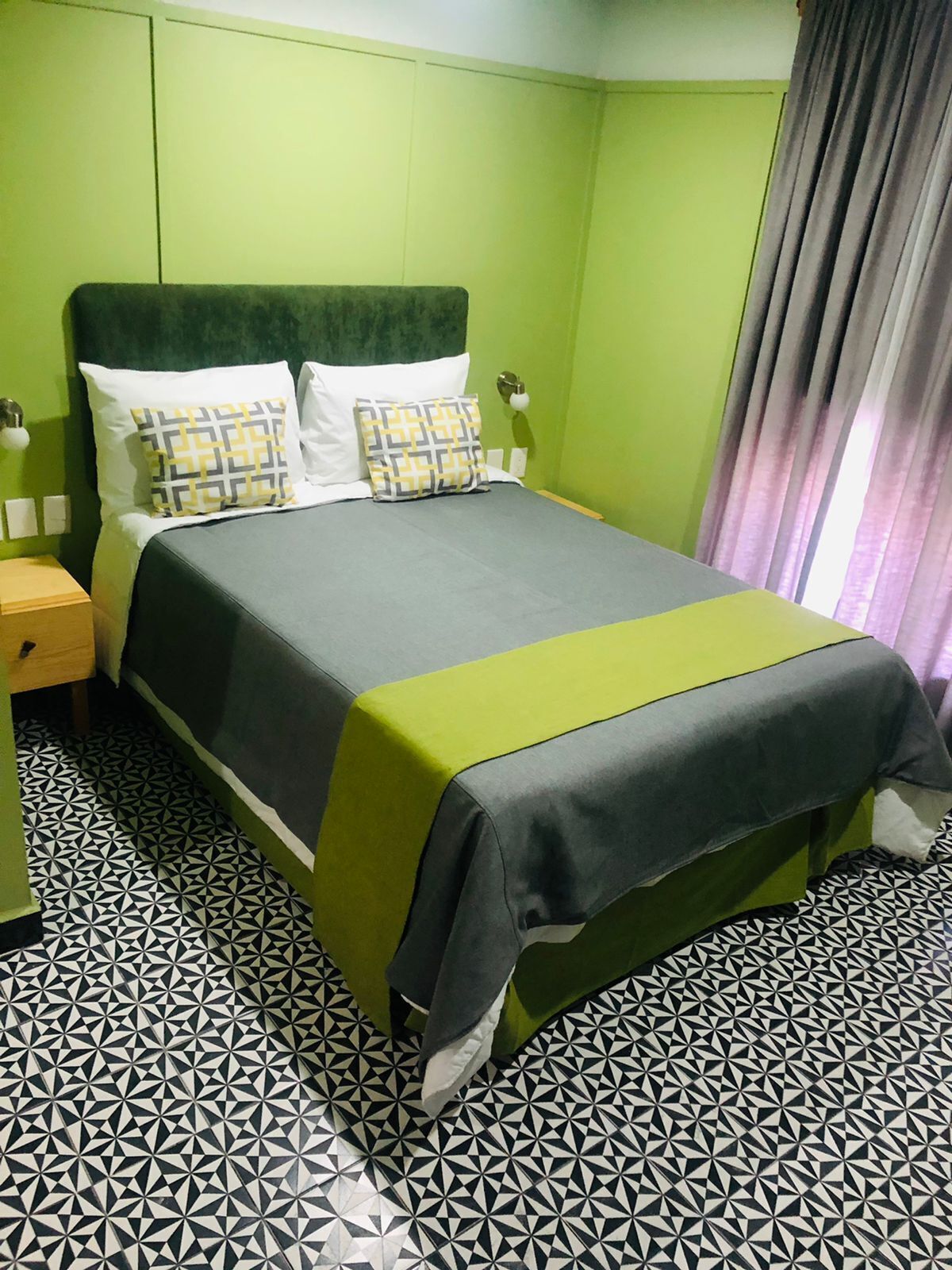 A hotel room with a bed, green walls, and patterned floor tiles.