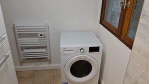 Een kleine wasruimte met een voorlader wasmachine, een droogrek en een raam met houten kader.
