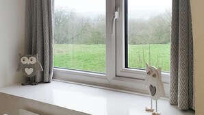 Ein Fenster mit Blick auf ein Wiesenfeld und Bäume, Vorhänge und zwei Eulen auf dem Fensterbrett.
