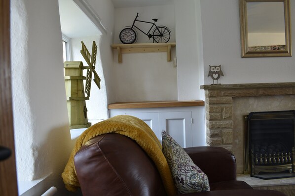 Ein Wohnzimmer mit braunem Ledersofa, einer gelben Decke, einem gemusterten Kissen, einem Holzregal mit einem Fahrrad, einer an der Wand befestigten Eulen-Dekoration und einem Kamin.