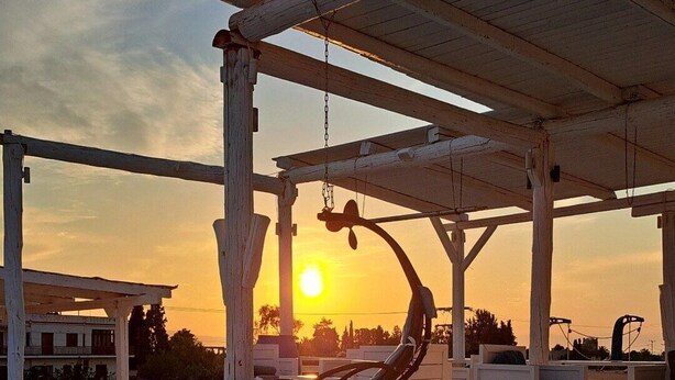 A pool area with a wooden pergola, lounge chairs, and a view of the sunset. - Nautilus (Aegina)