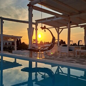 A pool area with a wooden pergola, lounge chairs, and a view of the sunset. - Nautilus (Aegina)