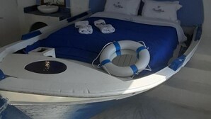 A boat-shaped bed with a blue headboard, white pillows, and a life preserver. - Nautilus (Aegina)