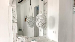 A bedroom with a large mirror, two white wicker lamps, and a blue accent wall. - Nautilus (Aegina)
