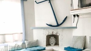 A cozy corner with a wooden table, a blue cushioned bench, and a decorative anchor on the wall. - Nautilus (Aegina)