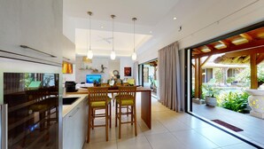 Cocina moderna con una isla central, iluminación colgante y vistas a una piscina y jardín.