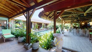 Un espacio al aire libre techado con piscina, sillones de descanso y mesas de comedor.