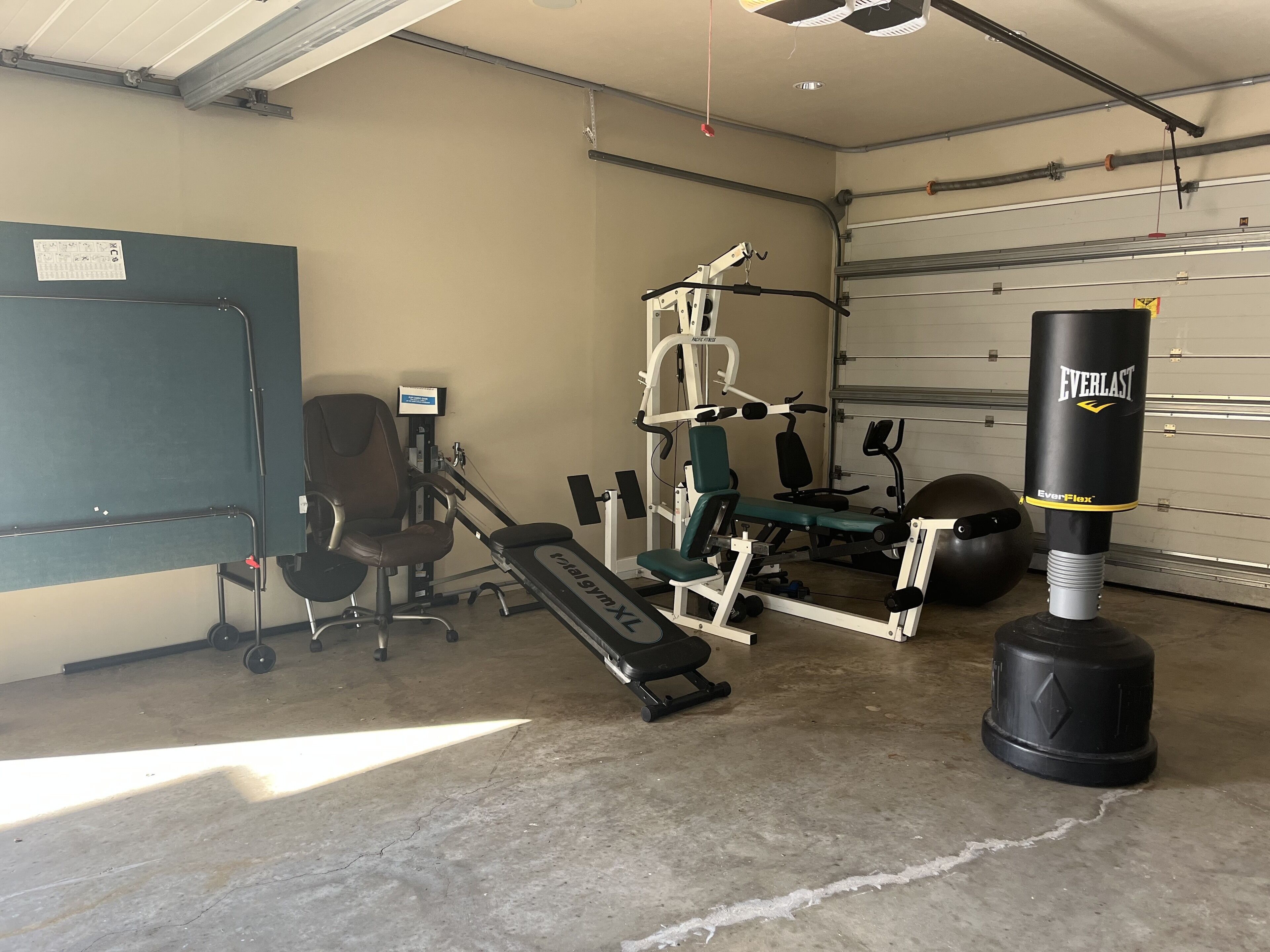 Une salle de sport équipée de matériel d’exercice, notamment un tapis de course, un banc de musculation et un sac de frappe.