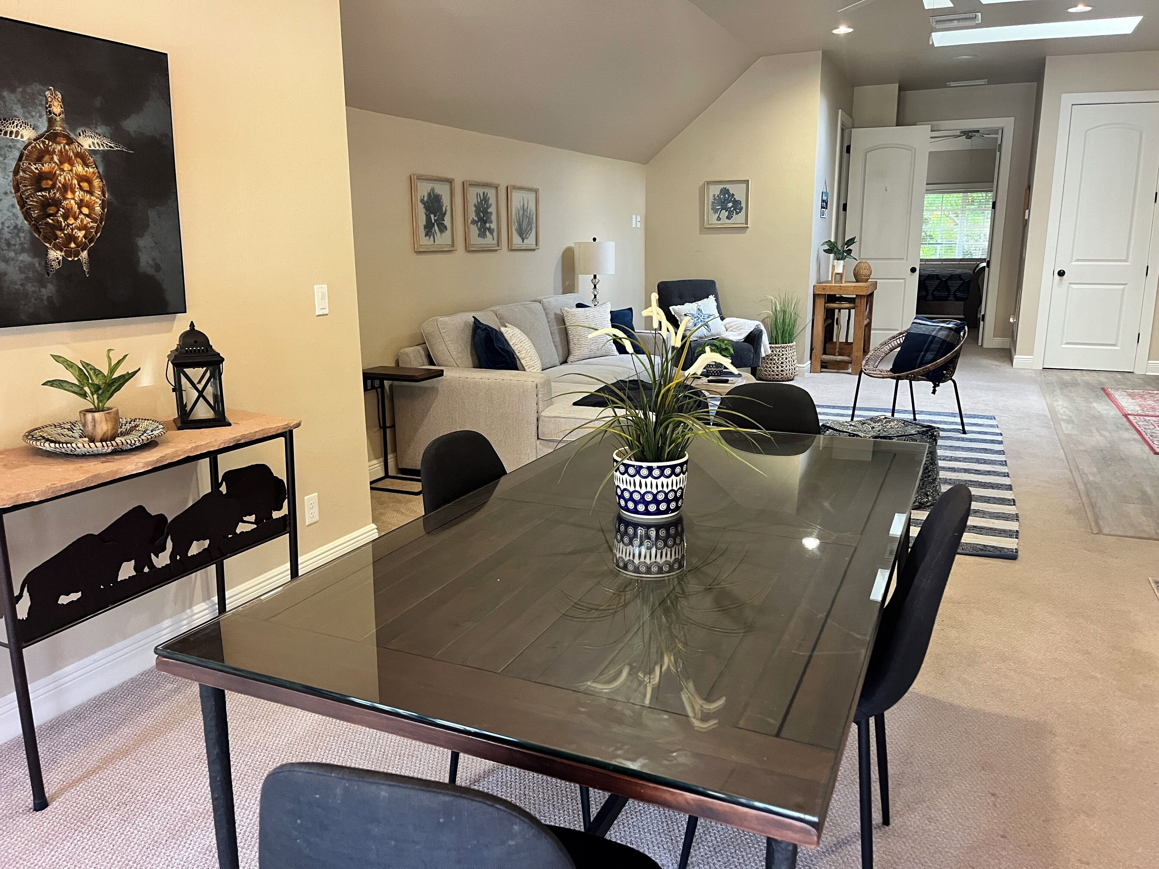 Un comedor moderno con una mesa de vidrio, sillas negras y un jarrón decorativo.