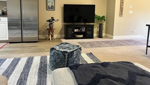 A living room with a large flat-screen TV, a refrigerator, a wooden coffee table, and a striped rug.