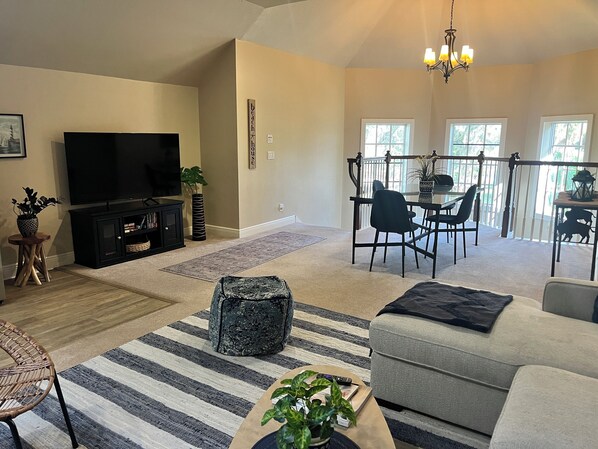 Relax in the spacious living room with a flat-screen TV, comfortable seating area, and dining space, plus a balcony with an outdoor view.