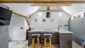 Une cuisine compacte dotée d’un îlot central, de tabourets en bois et d’un plafond avec des poutres apparentes.