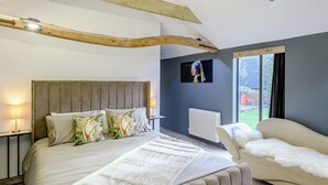 Une chambre à coucher comprenant un lit, un canapé, un téléviseur fixé au mur et une fenêtre donnant sur l’extérieur.