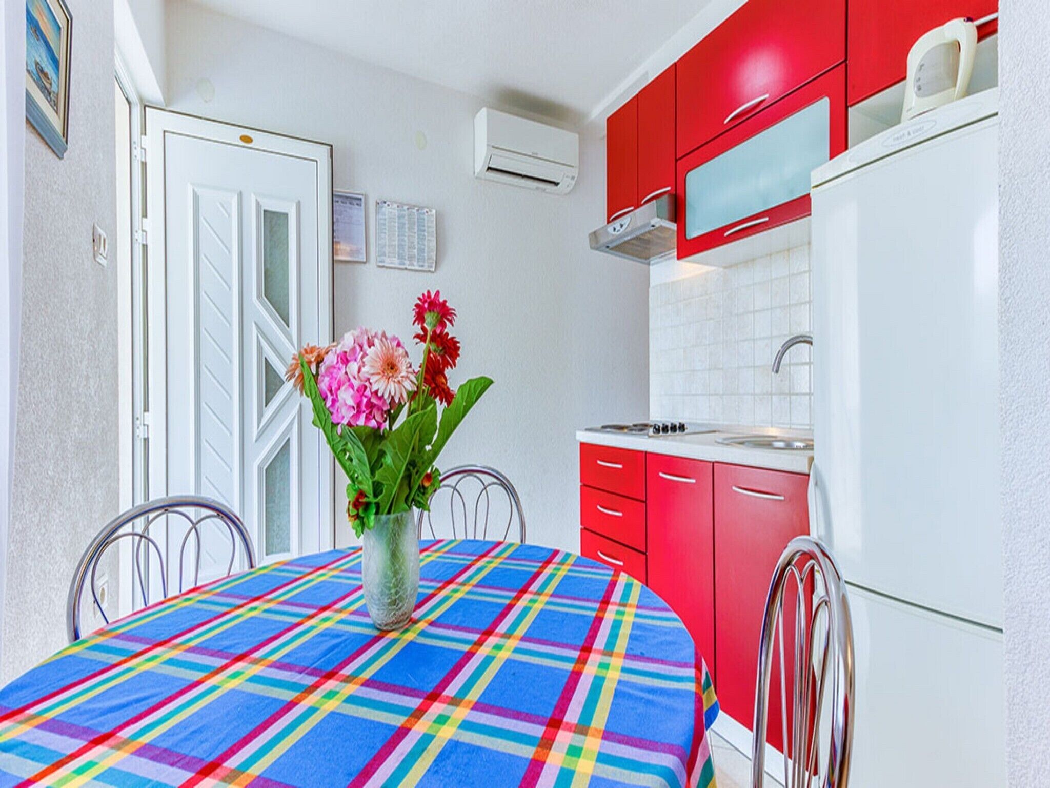 Una cocina con armarios rojos, un refrigerador blanco y un mantel colorido.