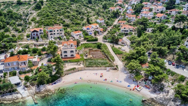 An aerial view of a coastal village with terraced houses, a sandy beach, and clear turquoise waters. - Apartments Ivo - Comfort One bedroom apartment with terrace and sea view (A3) (Postira)