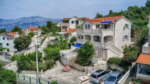A hillside residential area with houses featuring balconies, a stone pathway, and a view of the sea and mountains in the background. - Apartments Ivo - Comfort One bedroom apartment with terrace and sea view (A3) (Postira)