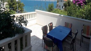 A balcony with a table and chairs, overlooking a coastal view with houses and mountains in the distance. - Apartments Ivo - Three bedroom apartment with terrace and sea view (A1) (Postira)