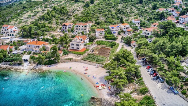 Eine Vogelperspektive auf ein Küstendorf mit terrassenförmig angelegten Häusern, einem Sandstrand und klarem türkisblauem Wasser.