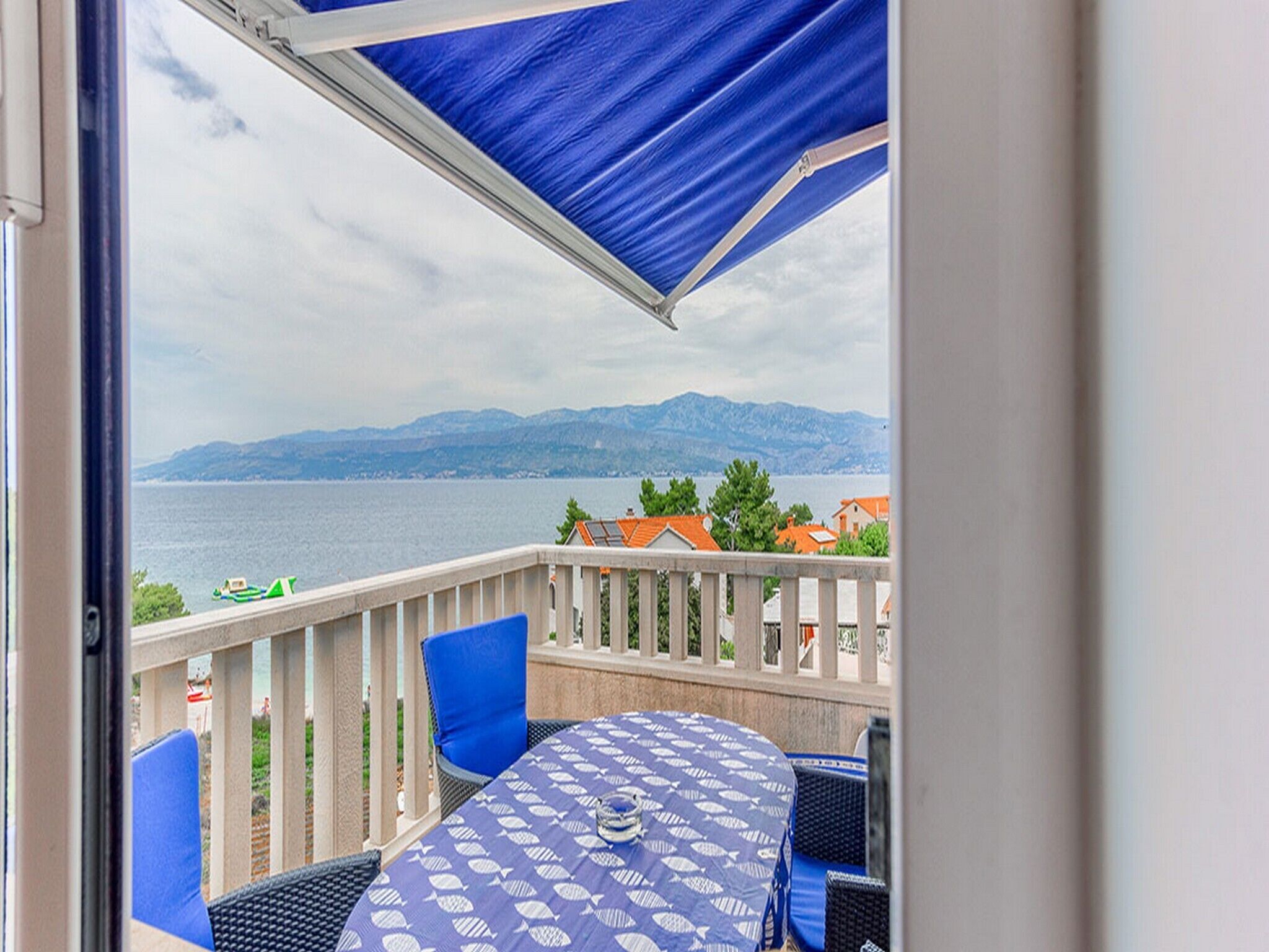 A balcony with a table and chairs, overlooking a body of water and distant mountains.