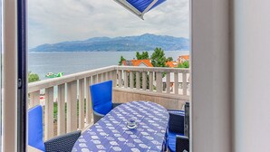 Ein Balkon mit Tisch und Stühlen, der auf ein Gewässer und ferne Berge blickt.