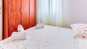 Ein Hotelzimmer mit einem Holzschrank, einem Bett mit floralem Bettbezug und einem Fenster mit durchsichtigen Vorhängen.