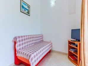 Un salón pequeño con un sofá rojo, un televisor sobre un mueble de madera y una estantería.