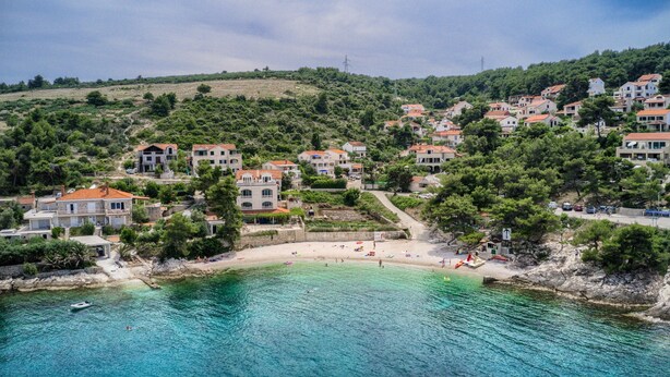 Un pittoresco villaggio costiero con case su una collina, una spiaggia e acque cristalline.