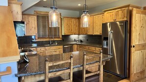 Una cocina con armarios de madera, refrigerador de acero inoxidable, encimeras de granito e iluminación colgante.
