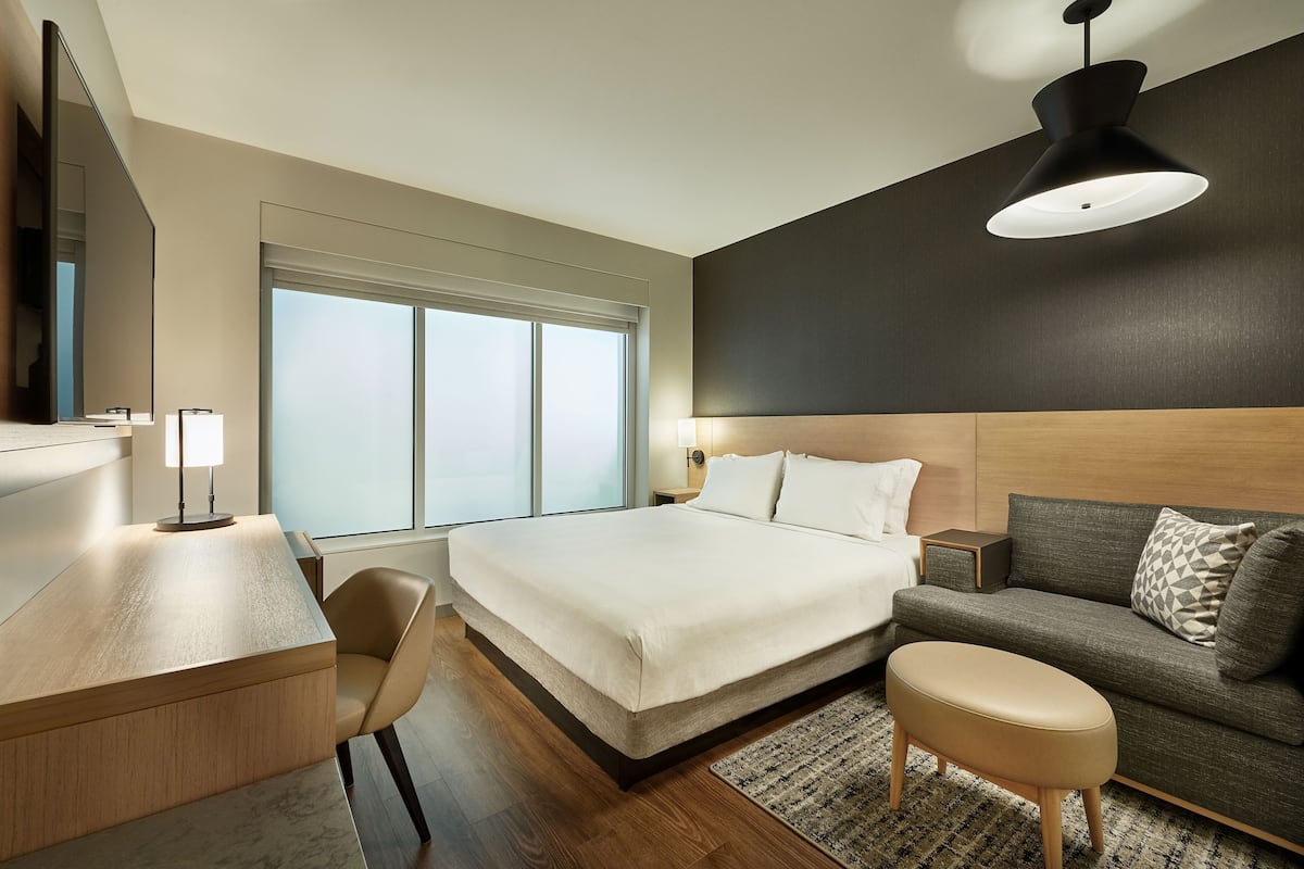 Een moderne hotelkamer met een bed, een bureau, een bank en een groot raam.