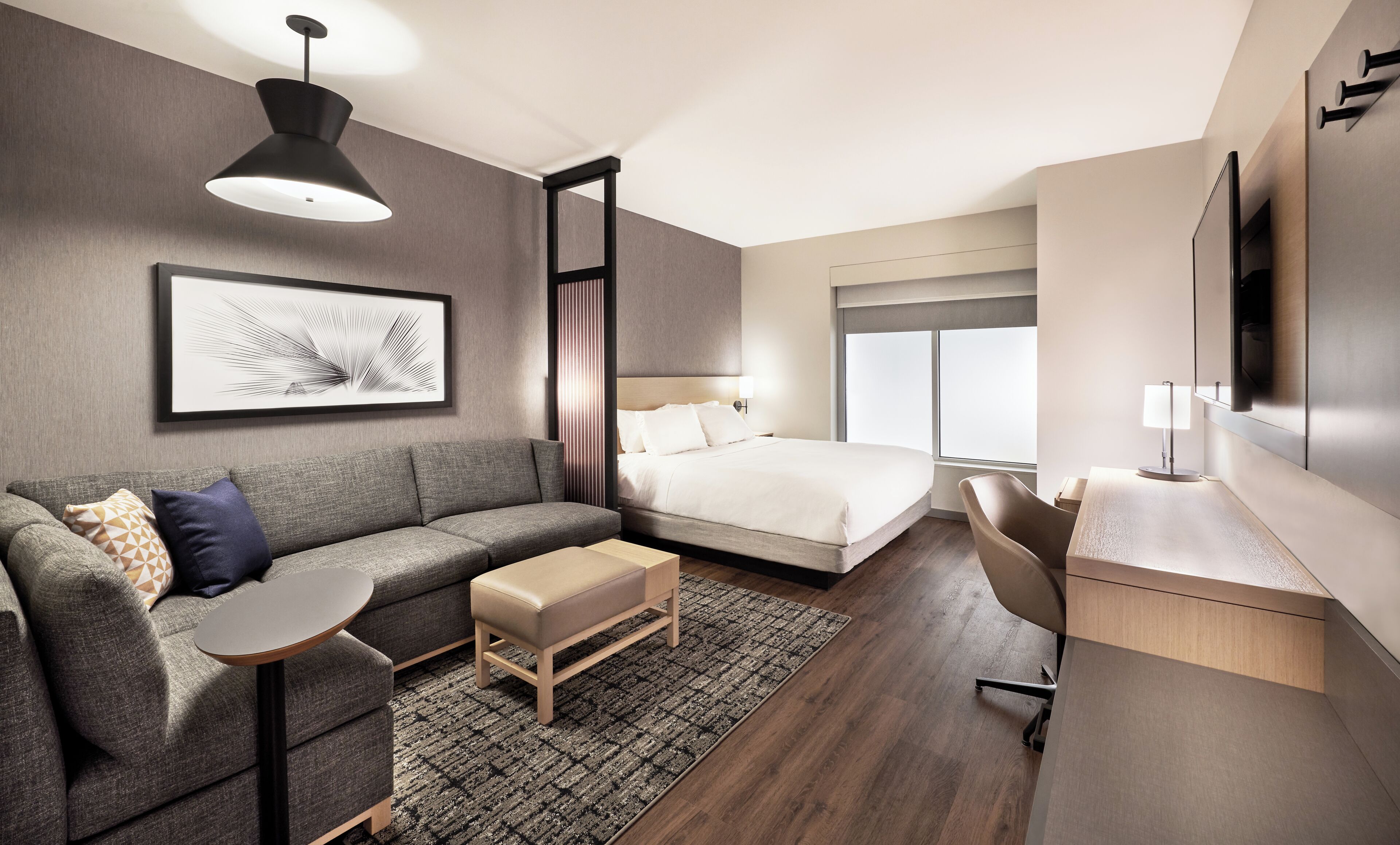 Una habitación de hotel moderna con cama, sofá, escritorio y un ventanal grande.