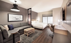 Una habitación de hotel moderna con cama, sofá, escritorio y un ventanal grande.