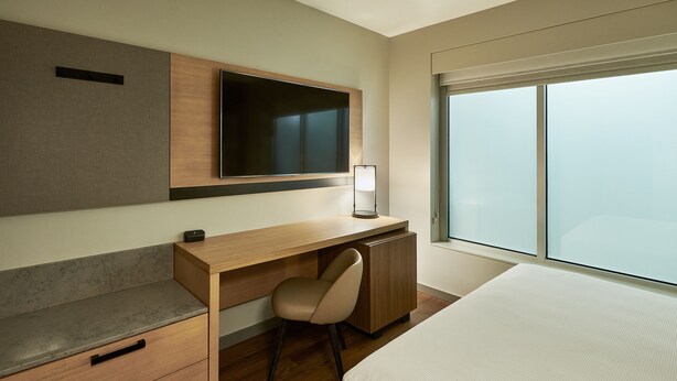 Une chambre d’hôtel moderne, dotée d’un bureau en bois, d’une chaise, d’un lit, d’une télévision et d’une grande fenêtre.