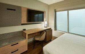 A modern hotel room with a wooden desk, a chair, a bed, a TV, and a large window. - Hyatt Place Asheville Airport (Arden)