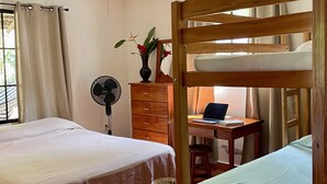 Una habitación con cama, un escritorio con una computadora portátil, un ventilador y un ventilador de techo.