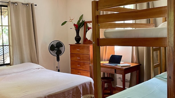 Ein Zimmer mit einem Bett, einem Schreibtisch mit einem Laptop, einem Ventilator und Deckenventilator.