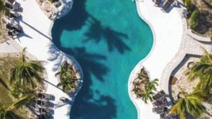 Oversigtsbillede af et resort med en stor central pool, omgivet af liggestole og palmer.