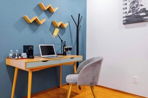 Ein modernes Zimmer mit einem Holztisch, einem Laptop, einem grauen Stuhl, einer Wandlampe und einem Wandbild.