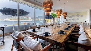 A dining area with a long wooden table, chairs, and hanging pendant lights. - Casa Luna del Mar - Private Pool & Beach, FastWifi (Puerto Vallarta)