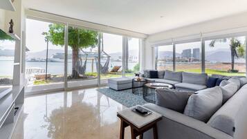 A spacious living room with a large window, a grey sofa, a small table, and a hammock.