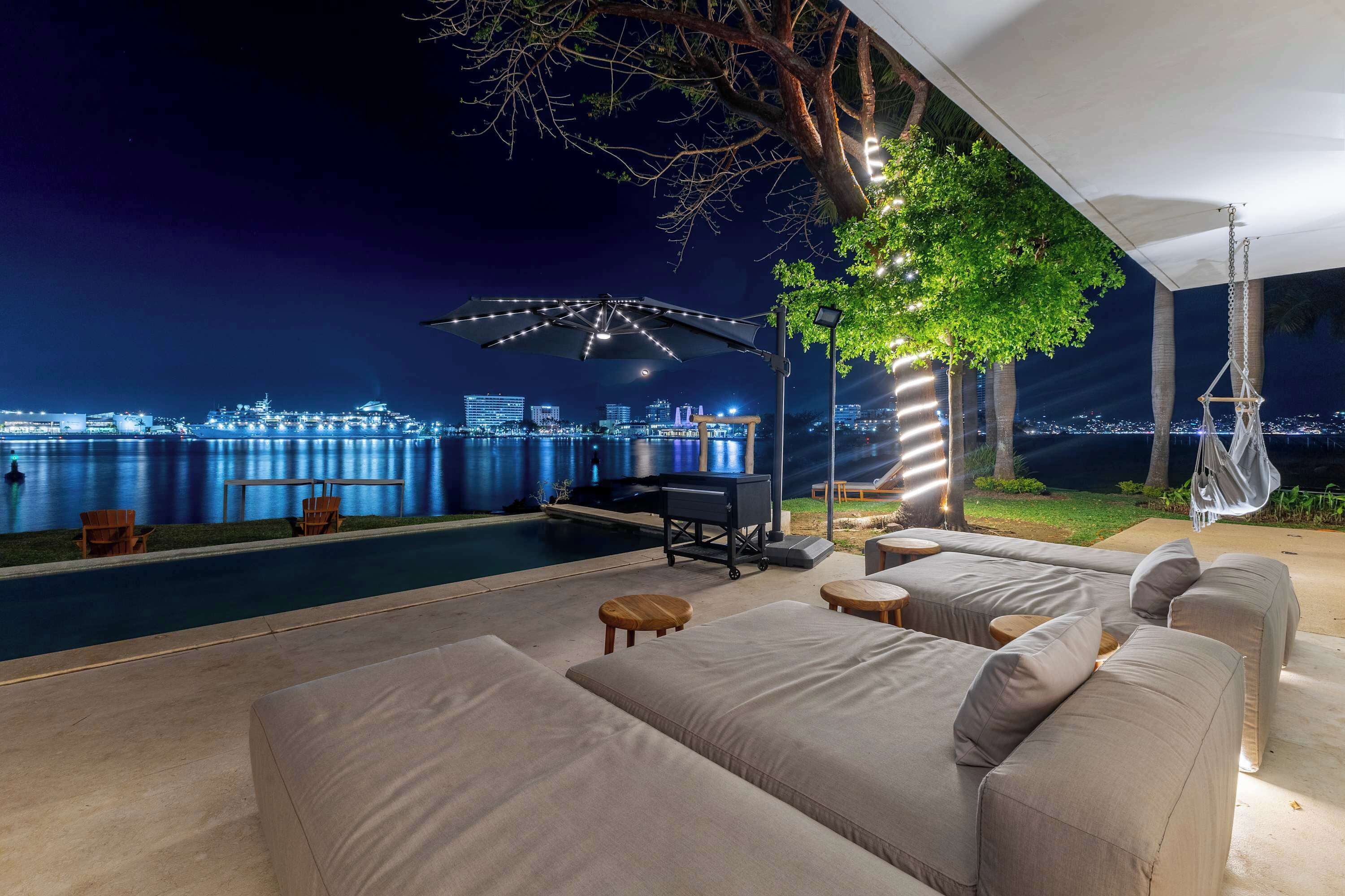 A poolside area with a sofa, chairs, and a grill.