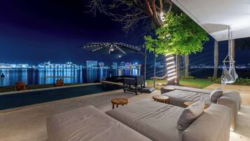 A poolside area with a sofa, chairs, and a grill.