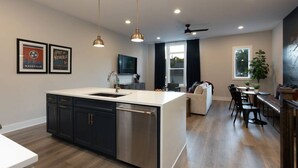 Une cuisine moderne dotée d’un îlot central, de meubles de couleur sombre, d’appareils électroménagers en acier inoxydable, de luminaires suspendus et d’un coin repas offrant une vue sur l’extérieur.